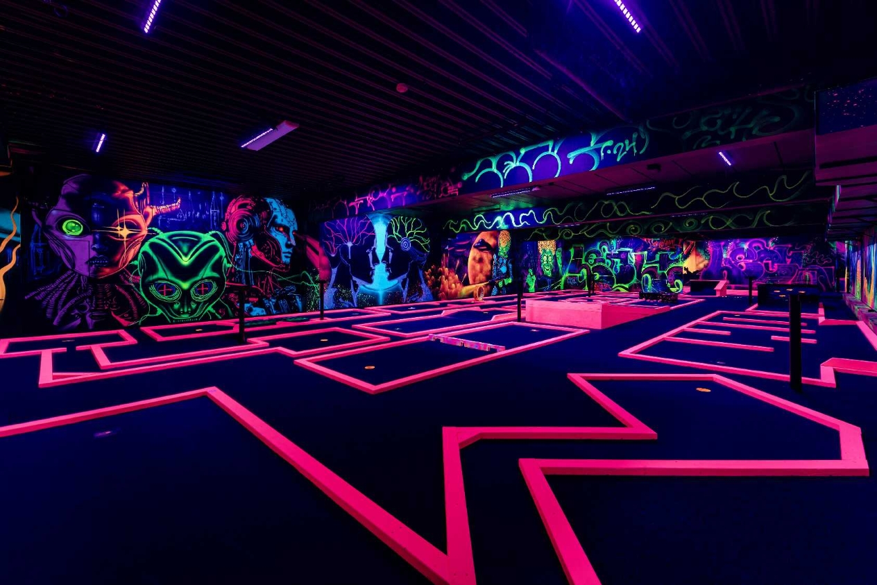 UV-minigolfen sett fra et annet perspektiv — neon-rosa baner som strekker seg innover, med veggmalerier i UV-fargene